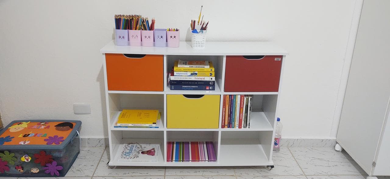 Estante branca com caixas coloridas, livros de psicologia e lápis de cor